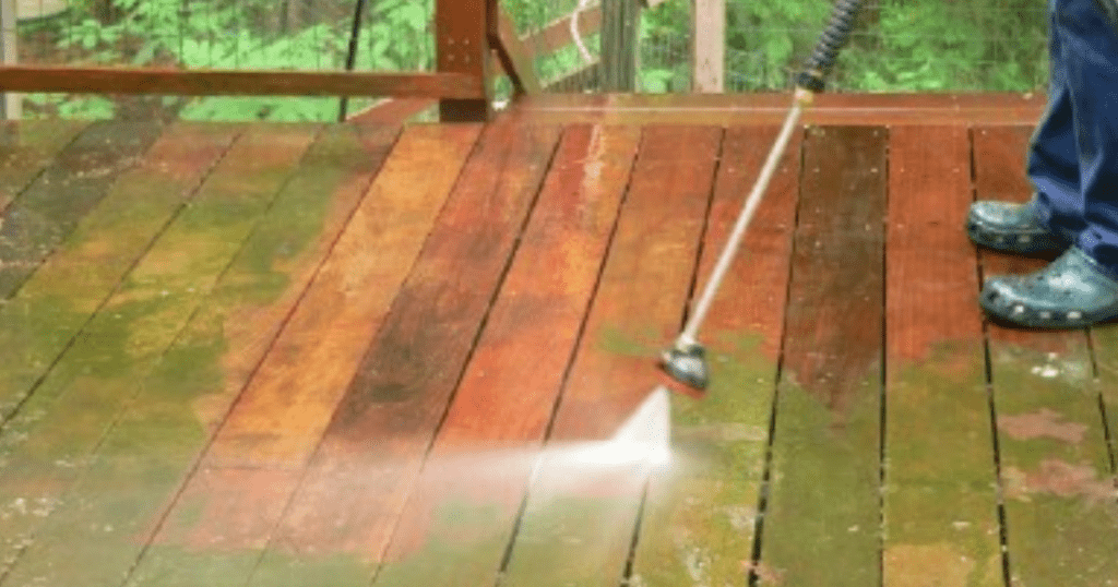 A person using a pressure washer to clean a composite deck. They are holding a wand with a nozzle, and directing the high-pressure water stream onto the deck surface.